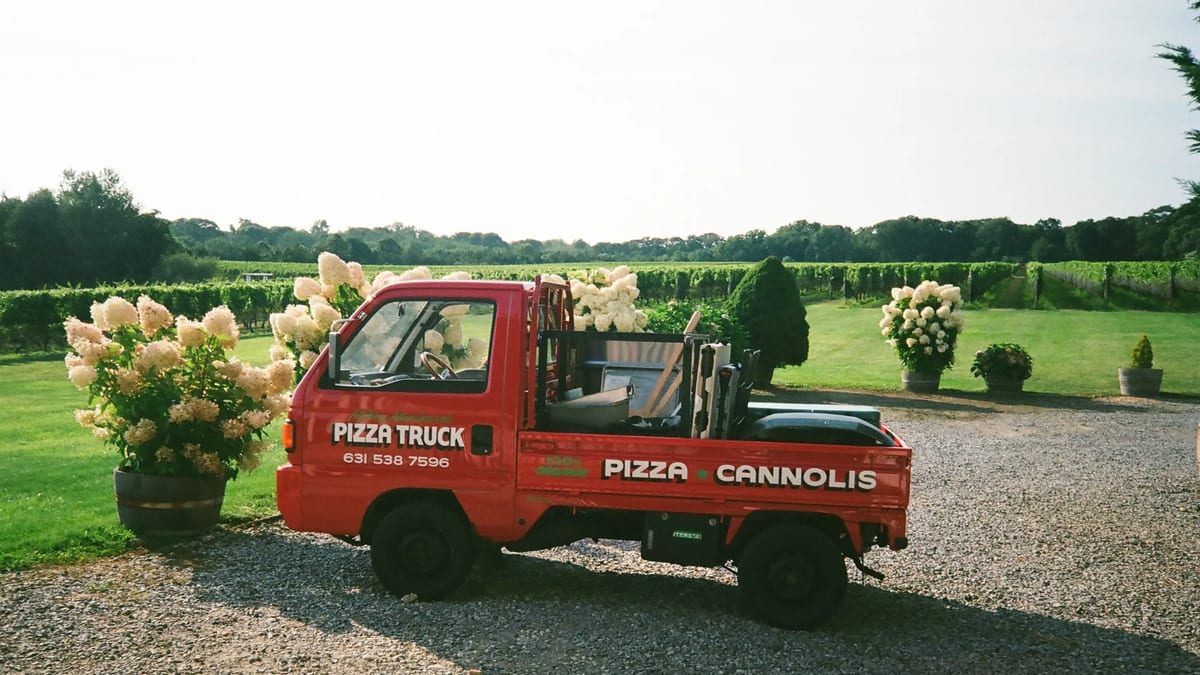 The red pizza truck parked on a gravel drive between hydrangea bushes