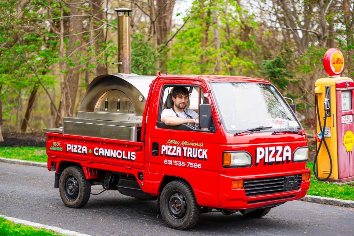 The pizza truck on the road with the wood-fired oven in the bed